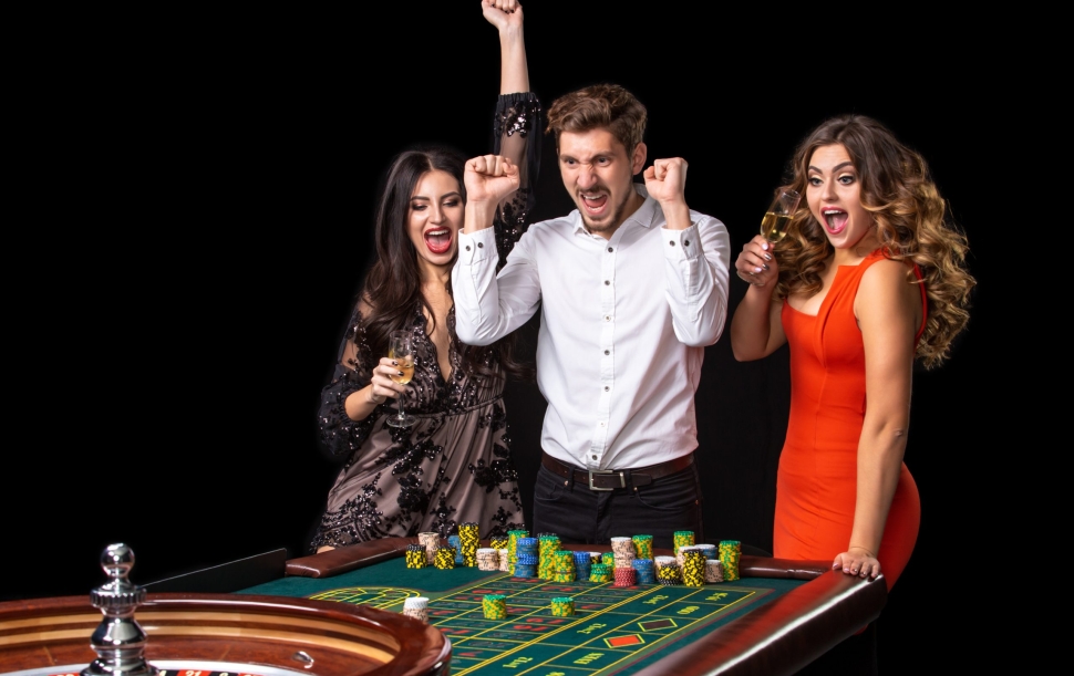 Group of young people looking excited at spinning roulette. Roulette table in a casino. Black background